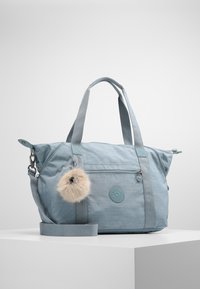 Sac fourre-tout en tissu bleu clair avec double poignées, une bandoulière amovible, une poche zippée à l'avant et un pompon en fourrure attaché.