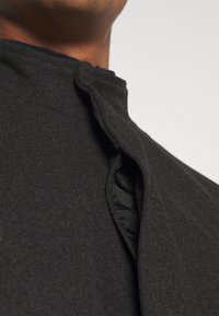 Cappotto nero in misto lana con collo alto, caratterizzato da una chiusura con bottoni e un tessuto morbido e strutturato. Vista ravvicinata del dettaglio del collo.