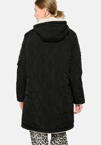 Čierna prešívaná zimná bunda s kapucňou a krémovým kožúškym golierom. Má diamantový vzor, dlhé rukávy a rovný lem.