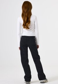 Schwarze gemusterte Jeans mit weitem Bein, mittelhoher Taille und Gesäßtaschen. Kombiniert mit einem weißen Longsleeve.