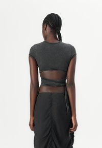 Top court en denim noir avec un dos transparent, associé à une jupe noire. Présente des manches courtes et une finition texturée.