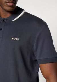 Μπλε polo πουκάμισο μεστεριανό γιακά και δύο κουμπιά, κλασικός γιακάς και αντίθετη λευκή ρίγα. Διαθέτει κεντημένο λογότυπο "BOSS" σε ανοιχτό χρώμα.