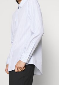Camicia a righe button-up in azzurro chiaro e bianco, con maniche lunghe, orlo arrotondato e polsini con bottoni. Tessuto di cotone con una trama liscia.