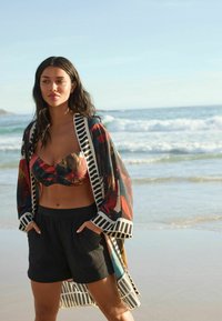 Black shorts and a floral-patterned, sheer kimono with striped accents. The top features twisted fabric and vibrant colors.