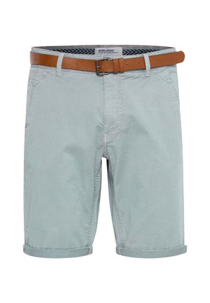 Short bleu clair jusqu’aux genoux, avec les ourlets retroussés, présenté avec une ceinture en cuir marron à boucle argentée.