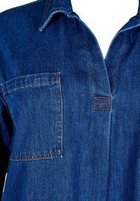 Sügavsinine teksashirt, millel on nööbid ja kaelus, rinnatasku ning kontrastsed oranžid õmblused õmblustel. Sile tekstuur.