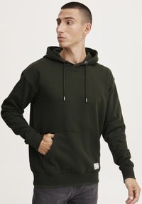 Felpa verde scuro con tasca frontale, cappuccio regolabile e polsini a coste. Realizzata in tessuto morbido con una superficie liscia.