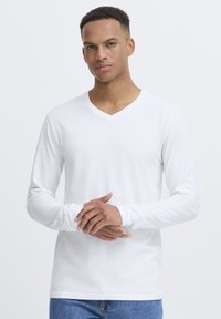 White long-sleeve V-neck t-shirt made of soft cotton, featuring a simple design with a smooth texture and fitted sleeves, paired with blue jeans.