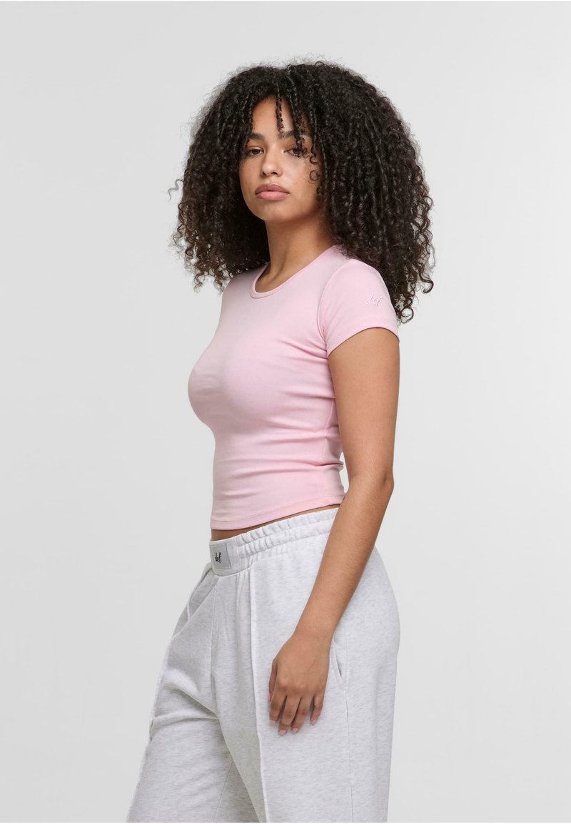 Kurzärmliges, eng anliegendes pinkes T-Shirt aus glattem Baumwollstoff, kombiniert mit grauen, locker sitzenden Sweatpants mit elastischem Bund.