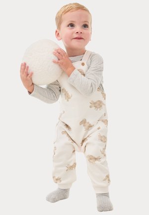 Weißer Overall mit hellbraunen Hasendrucken, Knopf-Schulter und weichem Material, kombiniert mit einem grauen Langarmshirt und grauen Socken.