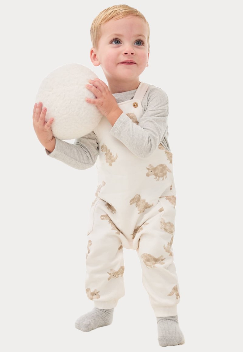 Weißer Overall mit hellbraunen Hasendrucken, Knopf-Schulter und weichem Material, kombiniert mit einem grauen Langarmshirt und grauen Socken.