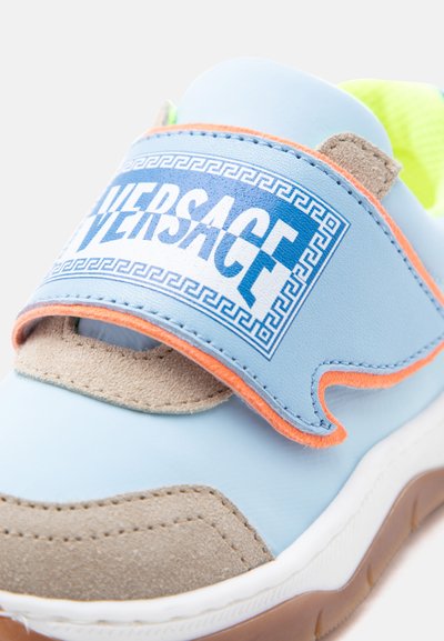 Ανοιχτό μπλε αθλητικό παπούτσι με γκρι σουέτ μύτη, πορτοκαλί περιθώριο, φθοριούχο κίτρινη επένδυση και ευρεία λουρίδα με μπλε λογότυπο "Versace" και μοτίβο ελληνικού κλειδιού.