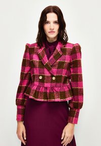 Vaaleanpunainen ja ruskea ruudullinen kaksirivinen lyhyt takki, jossa on peplum-helma ja kultasävytetyt napit. Teksturoitu kangas ja puffihihat.