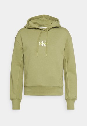 Oliivinvihreä huppari, jossa on kengurun tasku, kiristysnyöri huppussa ja resorit hihansuissa. Varustettu valkoisella "CK"-logolla ja "Vintage Jeans" -tekstillä.