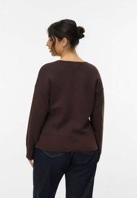 Brauner, übergroßer Sweatshirt mit weit ausgeschnittenem Halsausschnitt, gerippten Bündchen und lockerer Passform, kombiniert mit dunklen Jeans. Strukturiertes Material, lässiges Design.