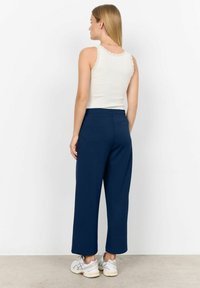 Navy wide-leg trousers made of soft fabric, paired with a white tank top featuring lace trim. Model wearing white and gray sneakers.