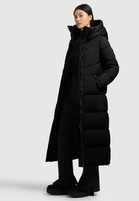 Čierna puffa bunda s dlhým, elegantným dizajnom, obsahujúca kapucňu, zips na prednej strane a bočné vrecká. Hladký, polstrovaný povrch s lesklým finišom.