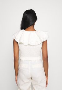 Top peplum branco com decote franzido e corpete com pregas, visto pela parte de trás. Textura suave com um tecido leve.