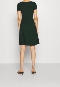 Robe verte à manches courtes, longueur genoux, en tissu doux avec un corsage ajusté et une jupe évasée, présentant un détail torsadé à l'arrière.