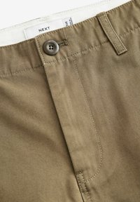 Pantaloni khaki con una texture liscia, dotati di chiusura con bottone, cintura cucita e etichetta all'interno della cintura.