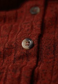 Gros plan sur un vêtement texturé marron avec un bouton en métal gravé du mot "SUPERDRY" au centre.