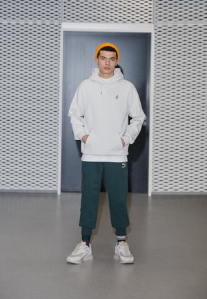 White hoodie with a front pocket and logo, paired with dark green cargo pants. Bright orange beanie and gray sneakers with white details.