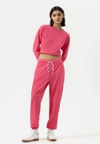 Roze cropped sweatshirt en bijpassende sweatpants van een lichtgewicht stof. De broek heeft een elastische tailleband en een trekkoord. Witte sneakers.