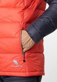 Rote und marineblaue Pufferjacke mit gesteppten Abschnitten, Reißverschlüssen an den Taschen und gesticktem "PREMIUM DOWN"-Logo. Weiches, isoliertes Material.