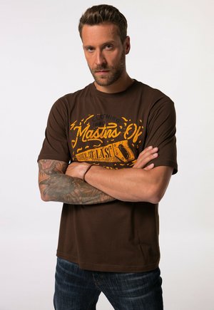 Brown cotton t-shirt with short sleeves, featuring yellow graphic text and designs. Worn with denim jeans, showcasing a relaxed fit.