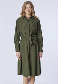 Abito verde in tessuto morbido, con colletto, maniche lunghe, chiusura con bottoni, cintura da annodare in vita e spacco laterale.