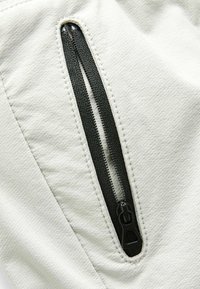 Tissu gris clair à texture fine, doté d'une poche zippée noire. La fermeture éclair possède un tirant lisse et un détail de couture caché.