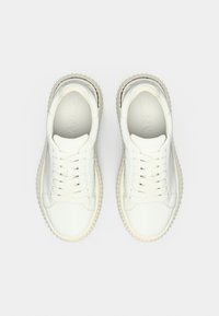 Άσπρα αθλητικά παπούτσια με υφασμένη επάνω επιφάνεια, στρογγυλή μύτη και επίπεδα κορδόνια. Διαθέτουν παχιά, ραβδωτή σόλα και διακριτική σήμανση στη γλώσσα.