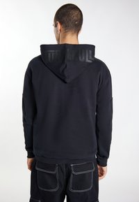 Zwarte hoodie met een gestructureerde achterkant met het "TUFF SKULL" logo. Glad materiaal, aansluitend ontwerp, geribde manchetten en een buidelzak.