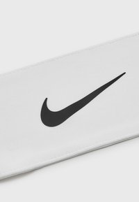 Valkoinen kangaspanta, jossa on näkyvä musta Nike-swoosh-logo. Pehmeä tekstuuri, siistit saumat ja yksinkertainen muotoilu.