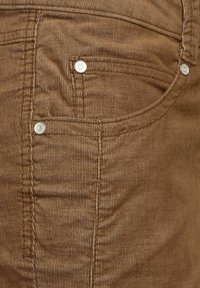 Brun manchester tyg i närbild, med horisontella ribbor, silverfärgade knappdetaljer och sömnadsdetaljer på framfickan.