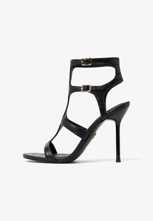 Sandale noire à talons hauts avec une texture faux-crocodile, dotée de deux accents de boucle et d'un design ouvert. Talon aiguille élégant.