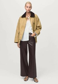 Khaki jacket with a black collar, white striped blouse, and brown wide-leg leather pants. Black sandals with minimal straps.