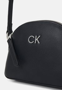 Borsa a tracolla in pelle nera con forma arrotondata. Presenta una cerniera argentata e un logo. Texture liscia con una leggera trama. Tracolla regolabile.
