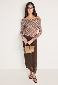 Hosszú ujjú, vállra eső blúz barna és bézs kockás mintával, barna, könnyed szoknyával és egy kis bézs retiküllel párosítva.