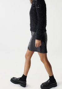 Černý chlupatý svetr s flitry na rukávech, v kombinaci s černou mini sukní z umělé kůže s texturovaným povrchem a bočními rozparky. Černé platformové loafer boty.