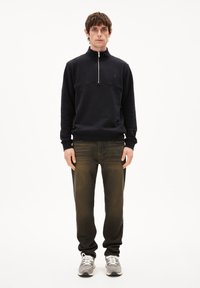 Sudadera con cremallera en color azul marino y cuello alto, de tela texturizada, combinada con jeans de mezclilla oscura y zapatillas grises con detalles en blanco.