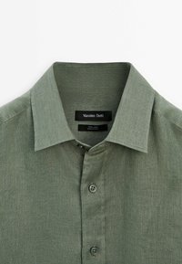 Groene linnen shirt met een standaard kraag, ronde knopen en subtiele textuur. Het label toont "Massimo Dutti" en verzorgingsinformatie.