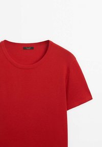 Chemise tricotée rouge à manches courtes et col rond, étalée à plat, montrant le haut de l'avant et les détails du col sur fond blanc.