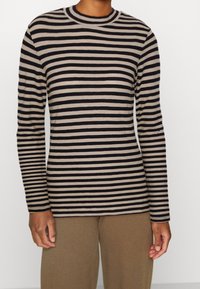 Stribet langærmet top i beige og sort. Rund halsudskæring, figursyet design, glat tekstur. Kombineret med løse beige bukser.