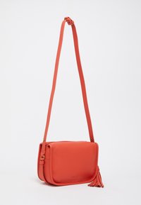 Korálová kožená crossbody taška s textúrovaným povrchom, obdĺžnikovým tvarom, nastaviteľným popruhom a strapcovým doplnkom na boku.