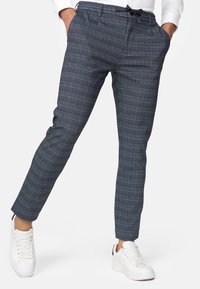 Pantalons à carreaux bleus et gris avec une coupe slim, taille élastique et détail à cordon de serrage, associés à des baskets blanches.
