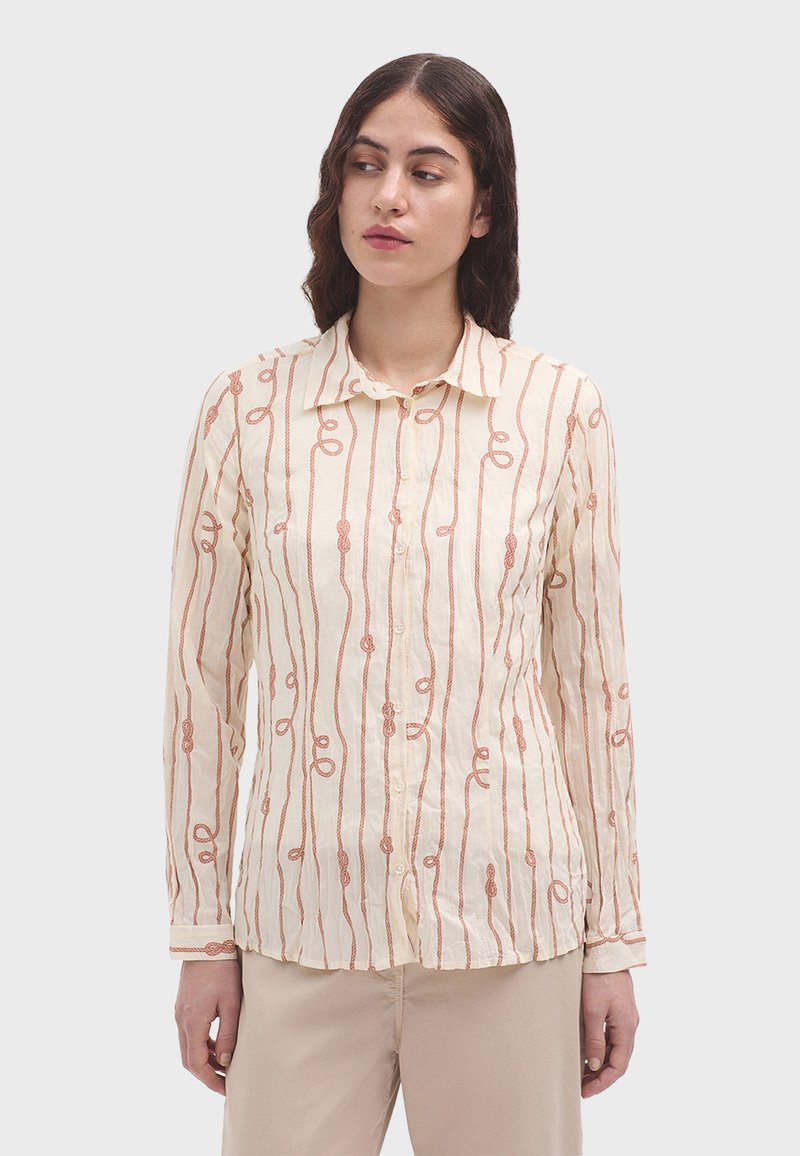 Camisa de manga larga color beige claro con cuello abotonado. Presenta una tela texturizada y un patrón de bucles naranjas repetitivos en toda la prenda.