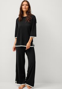 Sort loungewear-sæt med en afslappet top med trekvartærmer og kontrasterende hvid trim. Bukser med vide ben og slids ved kanten.