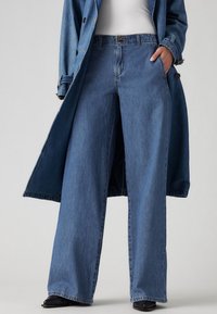 Laosihuiset tummansiniset farkut, joissa on korkea vyötärö, klassinen viisi-taskuinen muotoilu ja näkyvät ompeluyksityiskohdat.