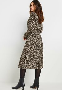 Abito avvolgente con stampa leopardata in toni beige e marroni, maniche lunghe, vita legata e orlo a metà polpaccio, abbinato a stivali neri alla caviglia.